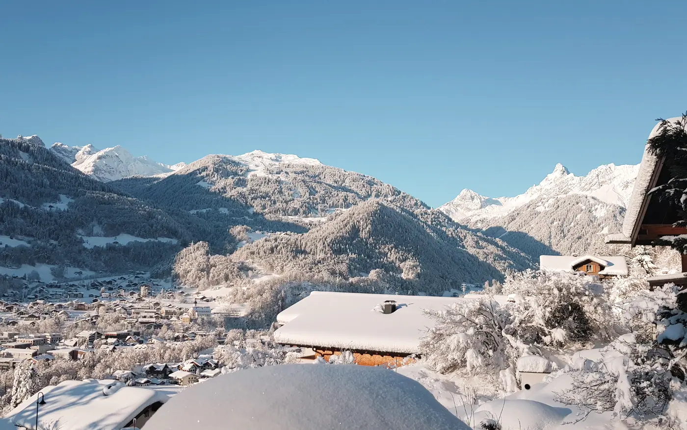 Verschneites Schruns mit Kirche und Bergen unter blauem Himmel, gesehen vom Hotel
